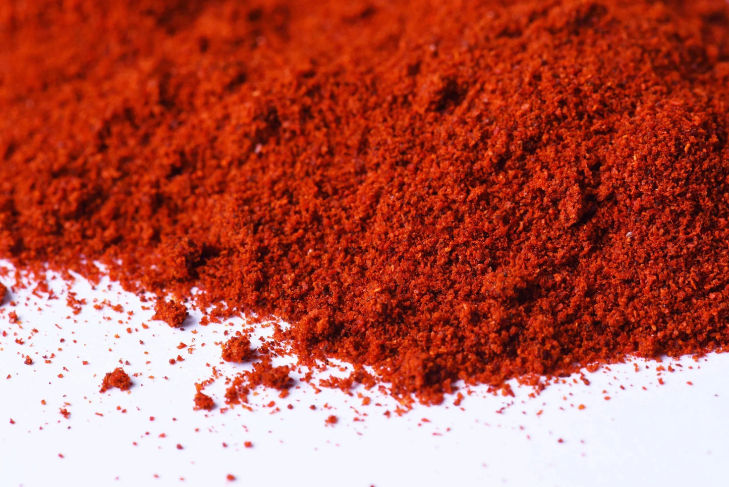 Close-up of vibrant red ground spice powder on a white surface