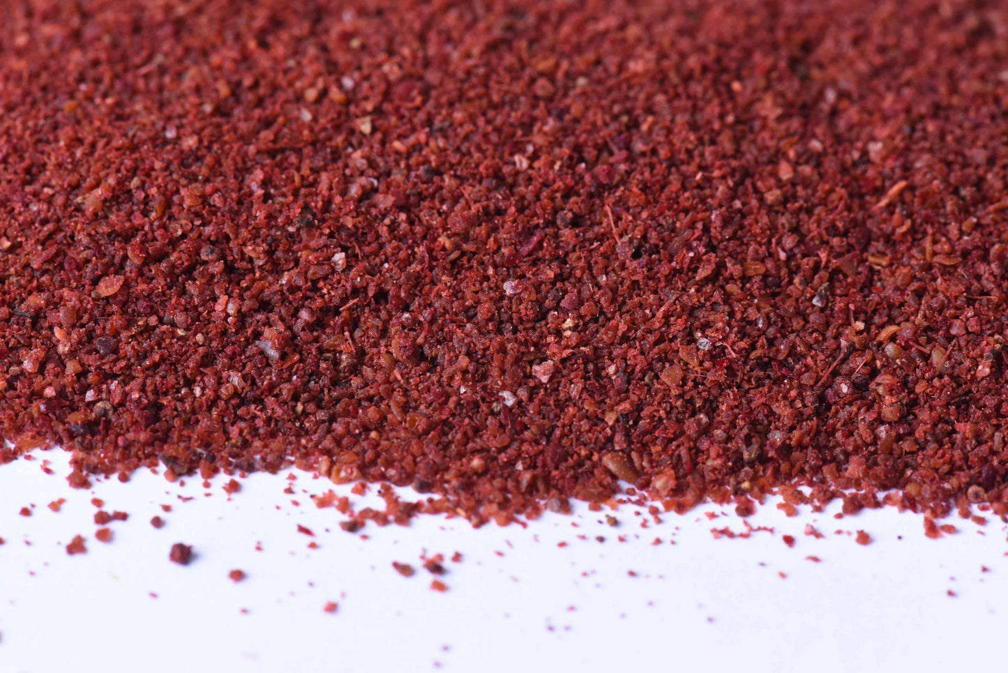 Close-up of coarse ground red sumac spice on white background for cooking and seasoning.