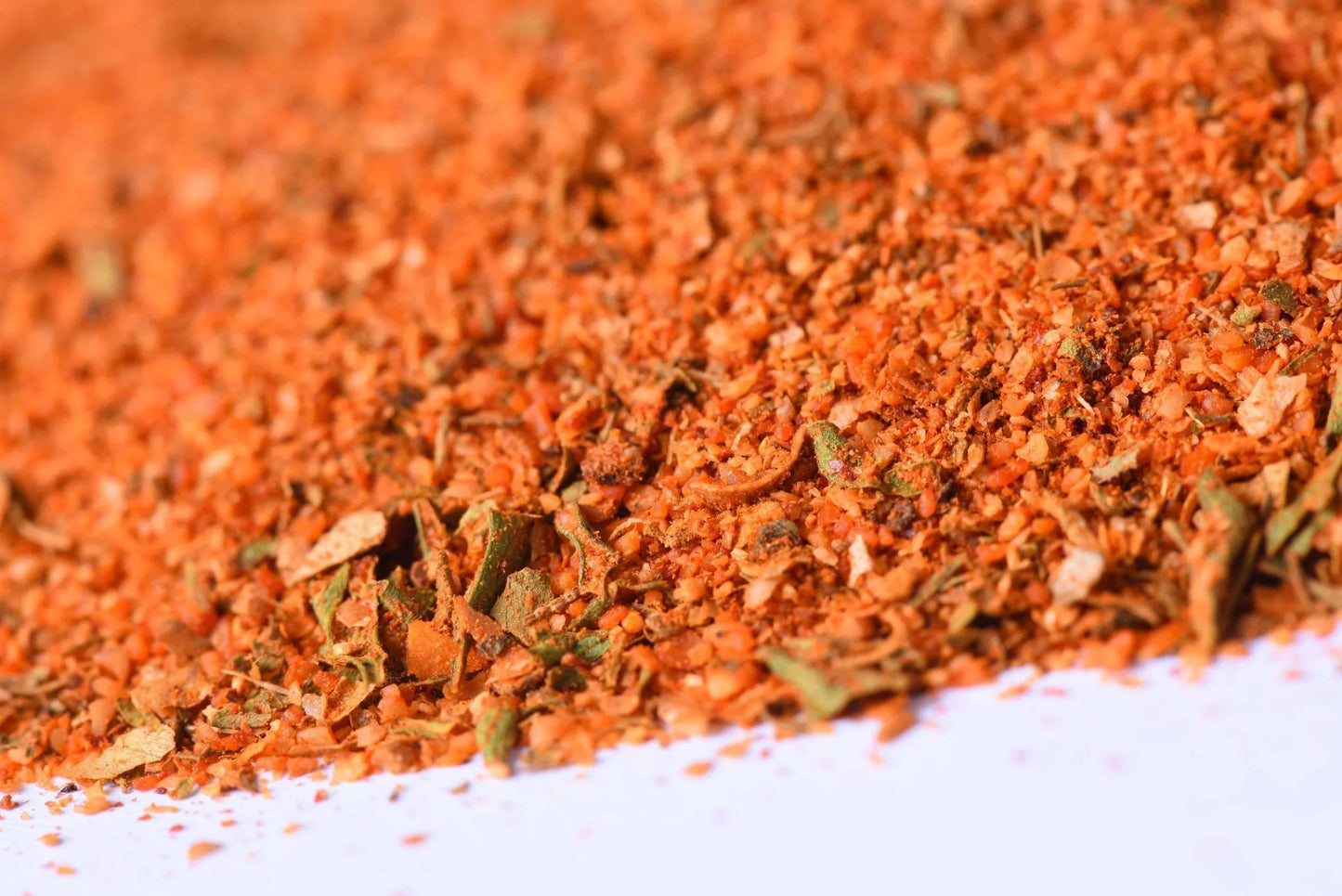 Close-up of coarse red-orange spice blend with herbs on a white surface