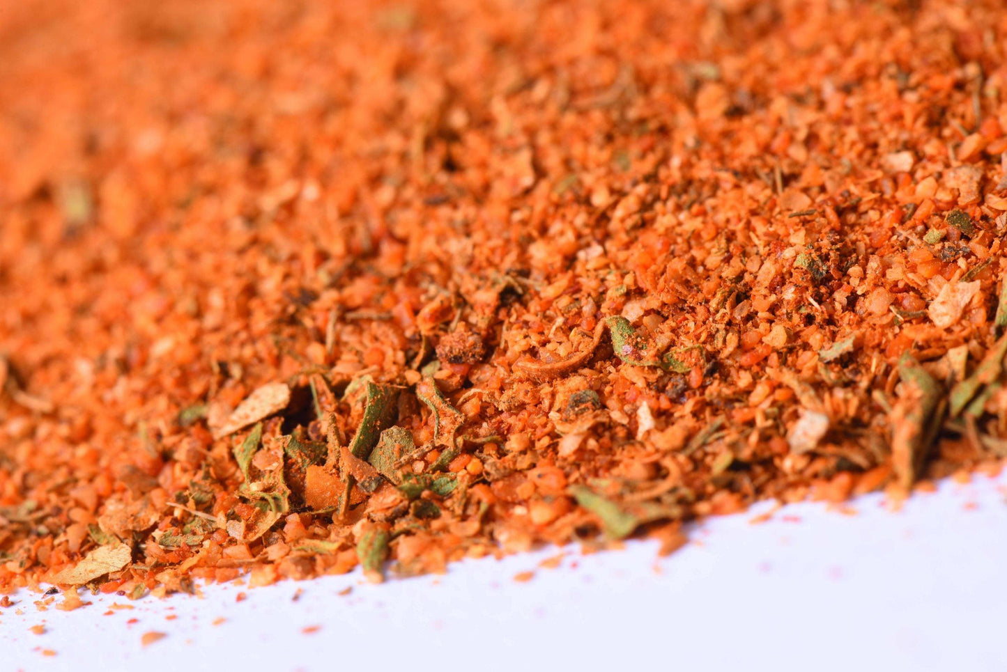 Close-up of coarse red-orange spice blend with herbs on a white surface