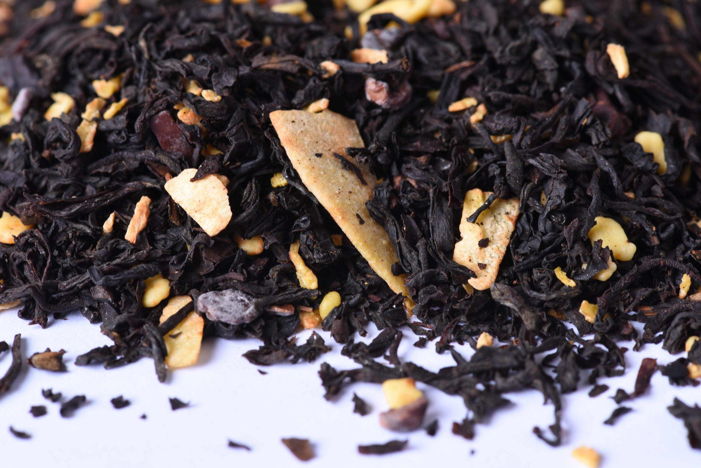 Loose-leaf black tea blend with dried fruit and nut pieces on a white surface