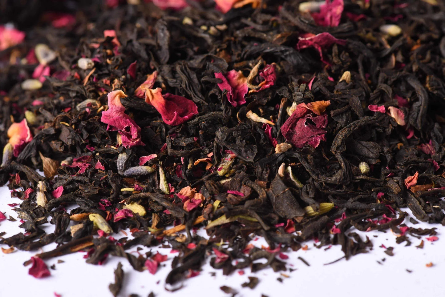 Loose leaf black tea blend with dried rose petals and spices on a white background