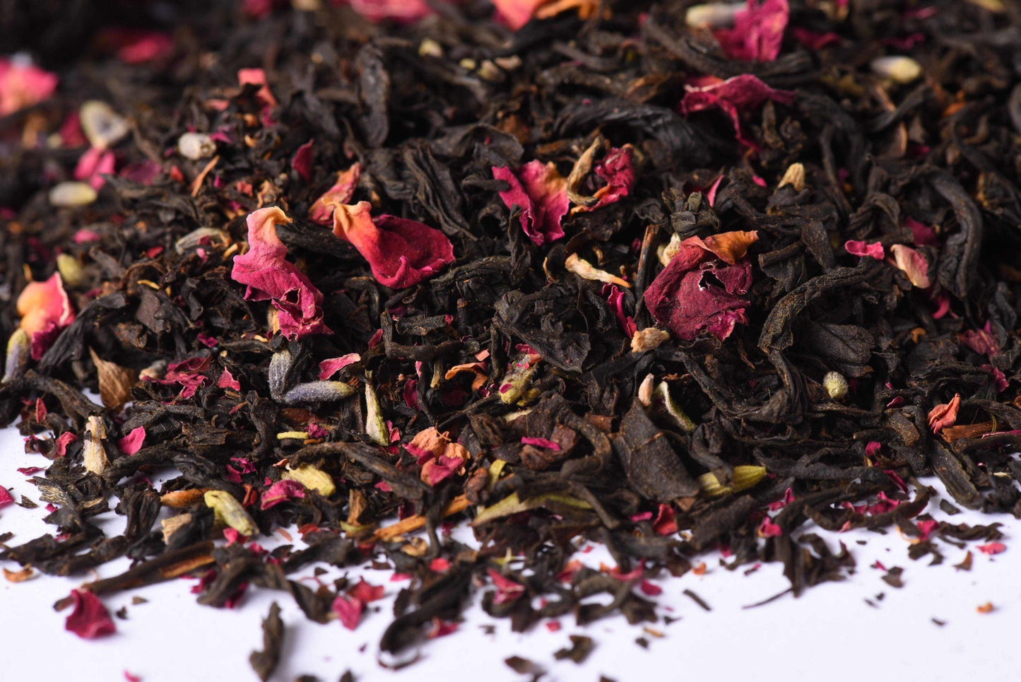 Loose leaf black tea blend with dried rose petals and spices on a white background