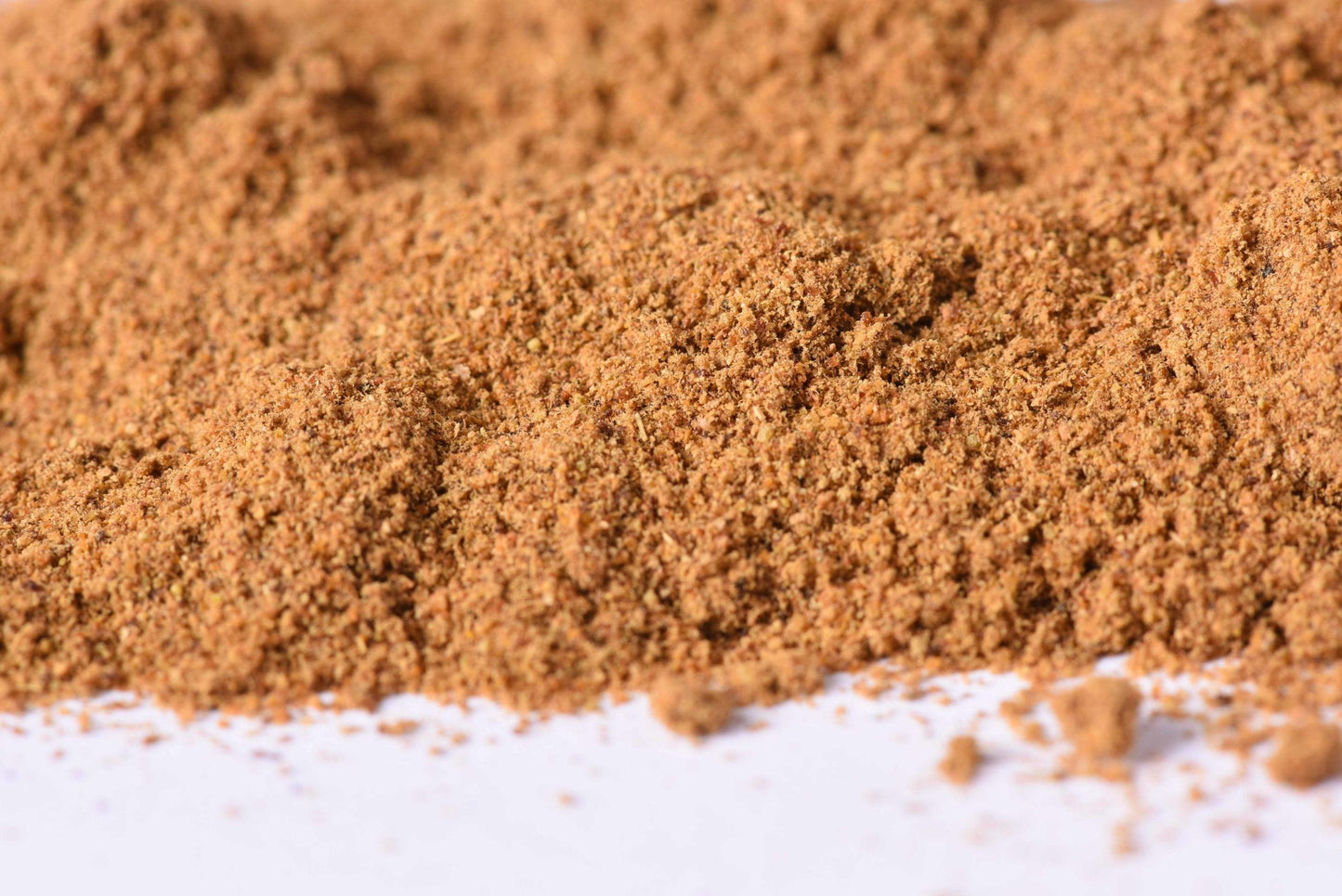 Close-up of a pile of ground spice blend, brown gourmet seasoning powder on white surface