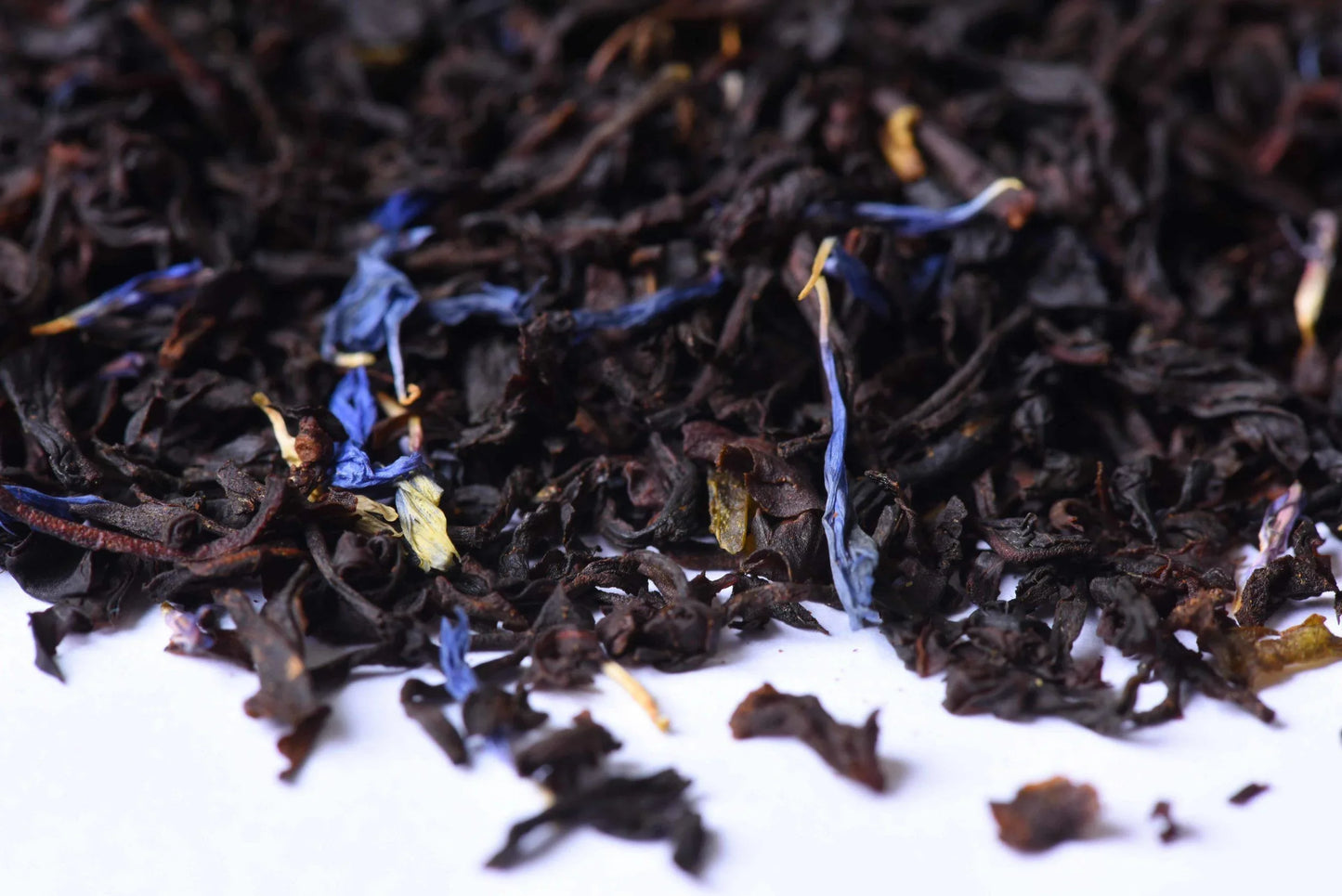 Loose leaf black tea blend with blue cornflower petals on a white background