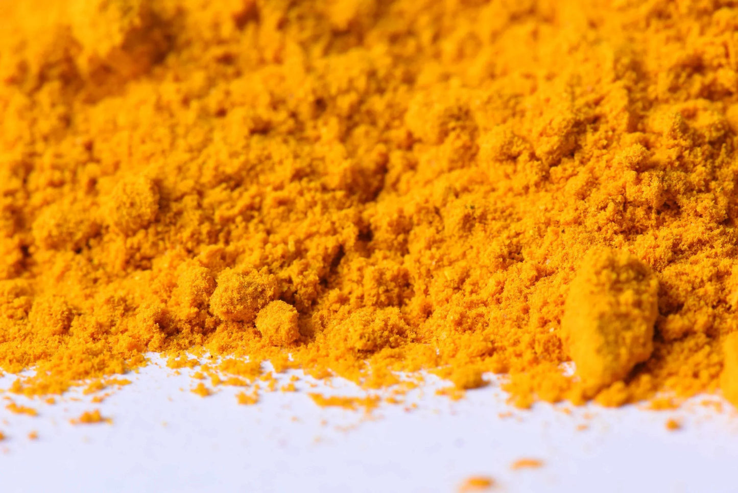 Bright yellow turmeric powder spice close up on white background