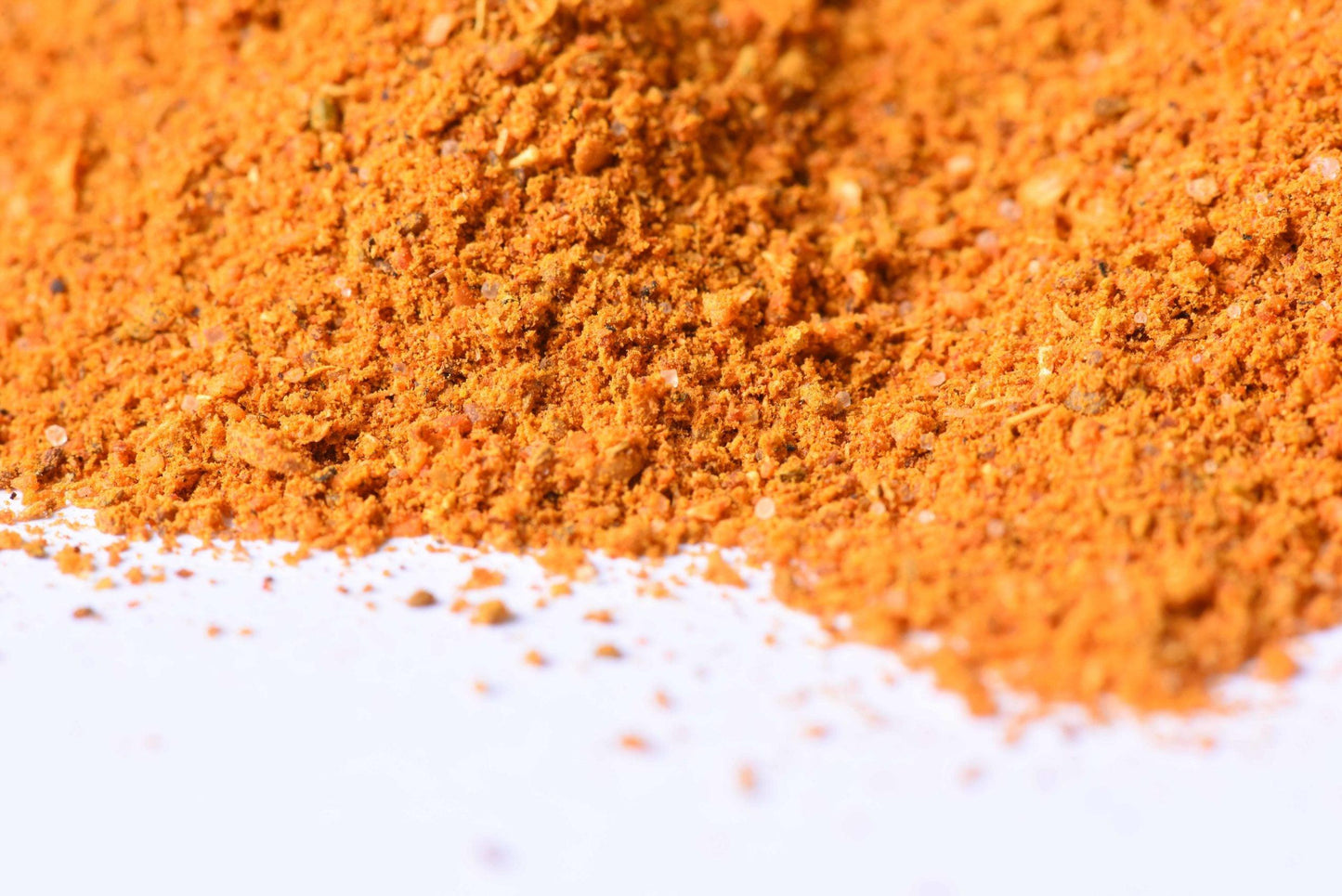 Close-up of orange spice blend powder on white background for cooking or grilling