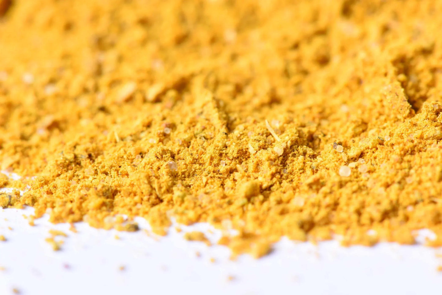 Close-up of bright yellow ground spice blend on a white surface