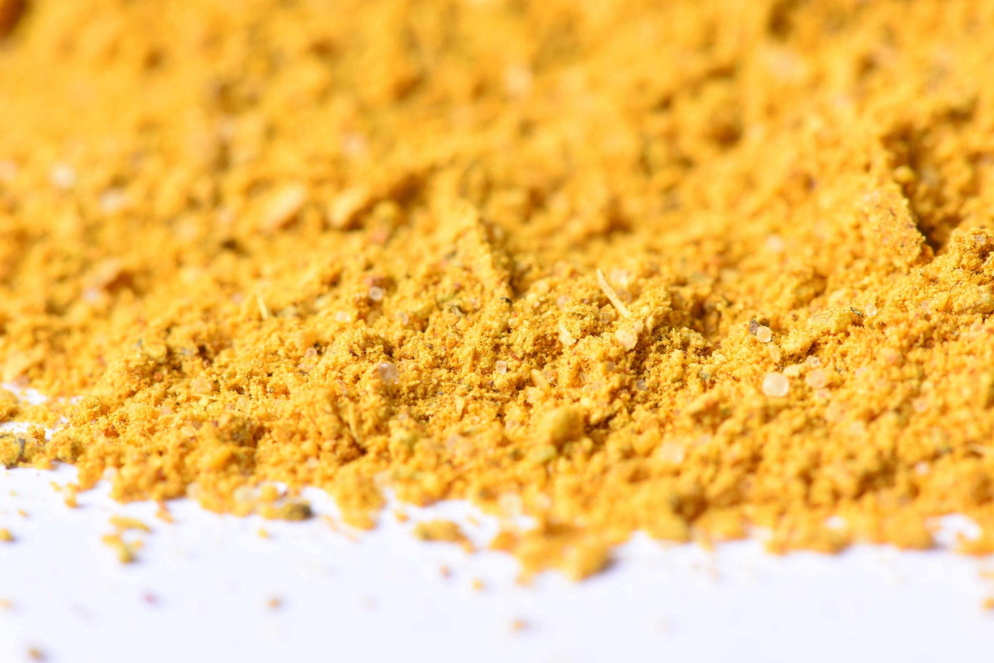 Close-up of bright yellow ground spice blend on a white surface