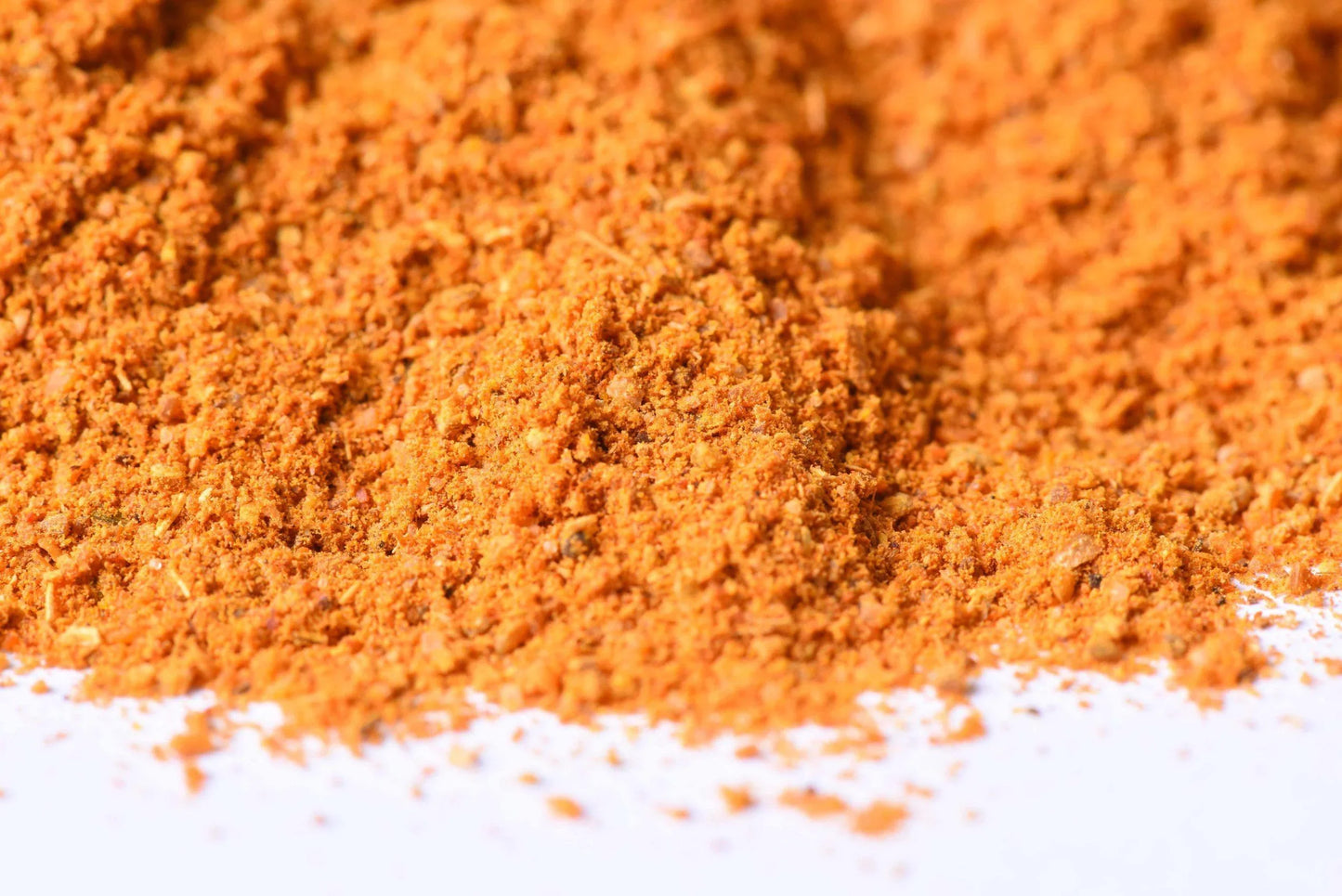 Close-up of a vibrant orange gourmet spice blend pile on a white surface