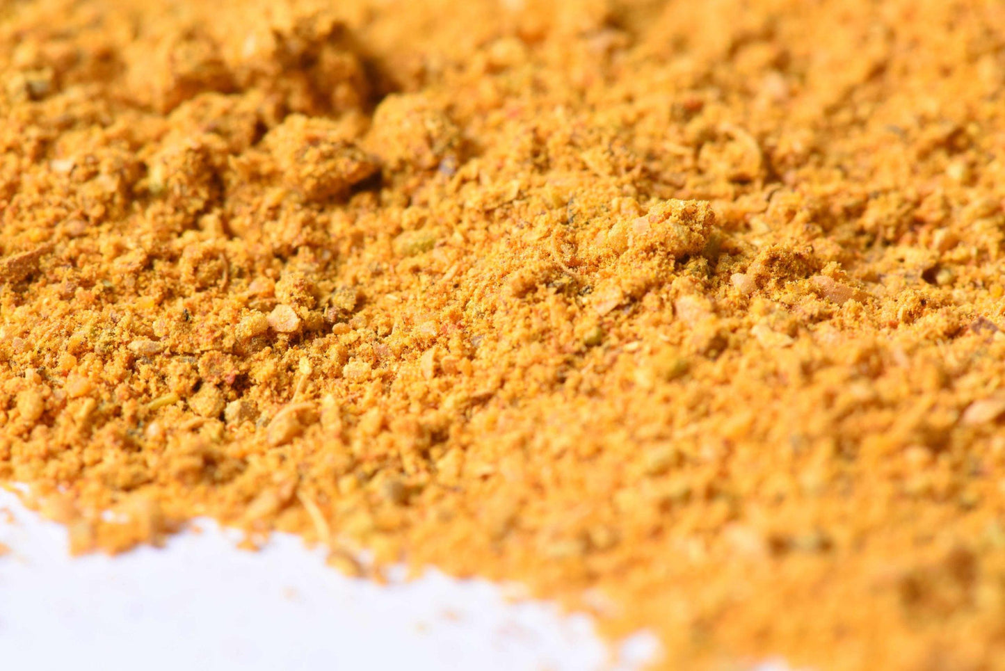 Close-up of yellow spice blend powder with fine and coarse texture on a white background.