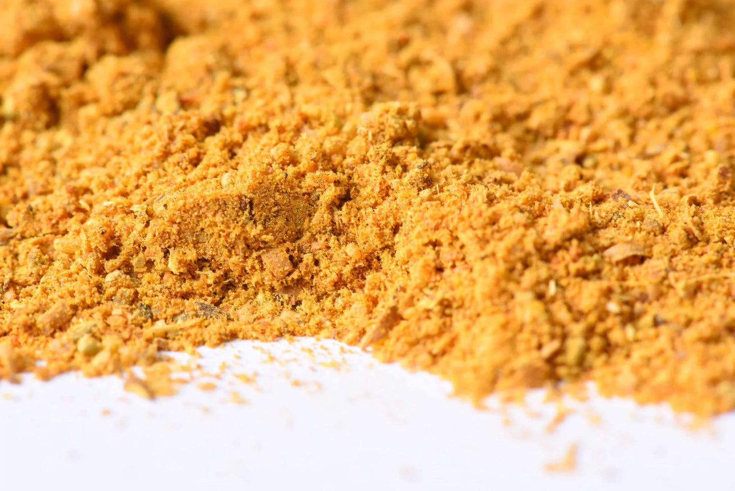 Close-up of golden yellow gourmet spice blend powder on a white surface