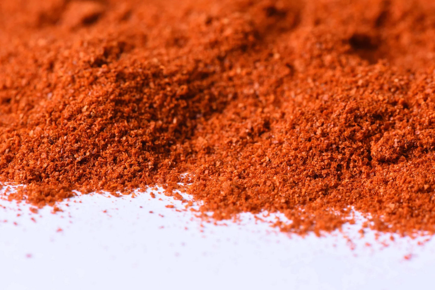 Close-up of vibrant red spice blend powder on a white surface