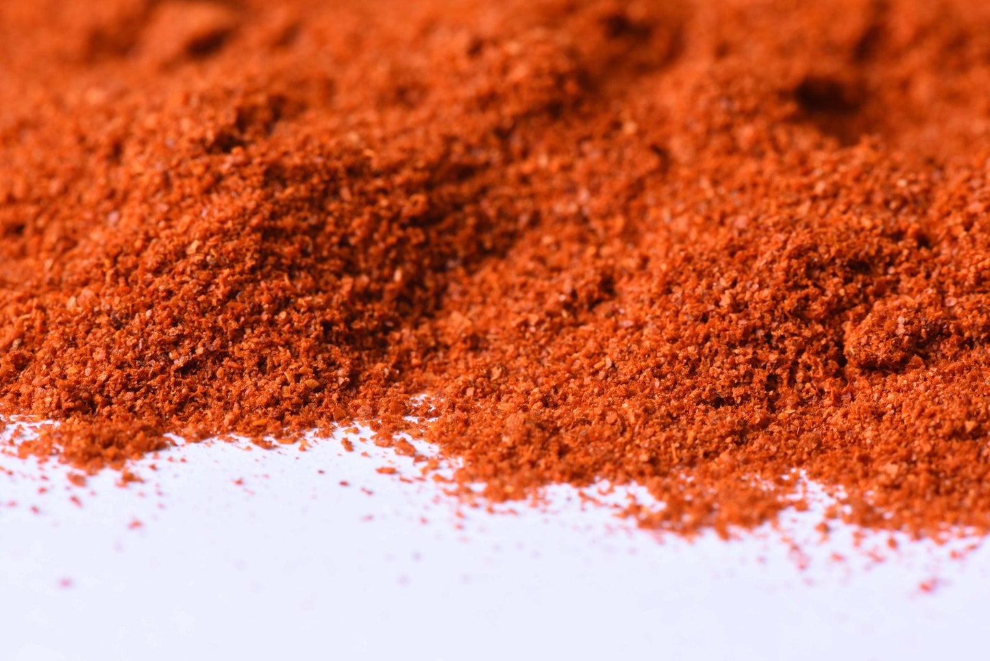 Close-up of vibrant red spice blend powder on a white surface