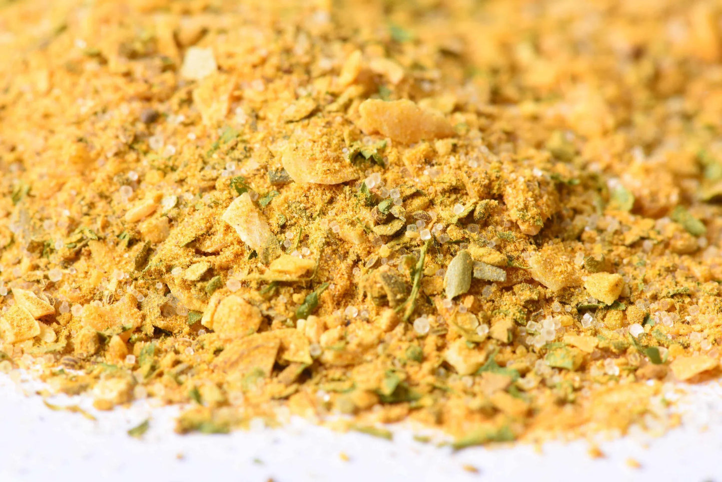 Close-up of a yellow gourmet spice blend with visible herbs and coarse salt granules