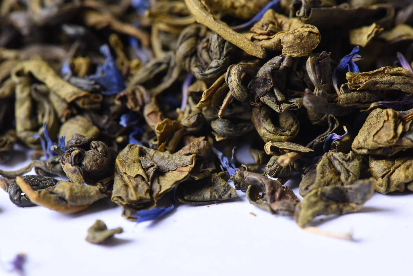 Loose-leaf green tea with dried blue petals on white background