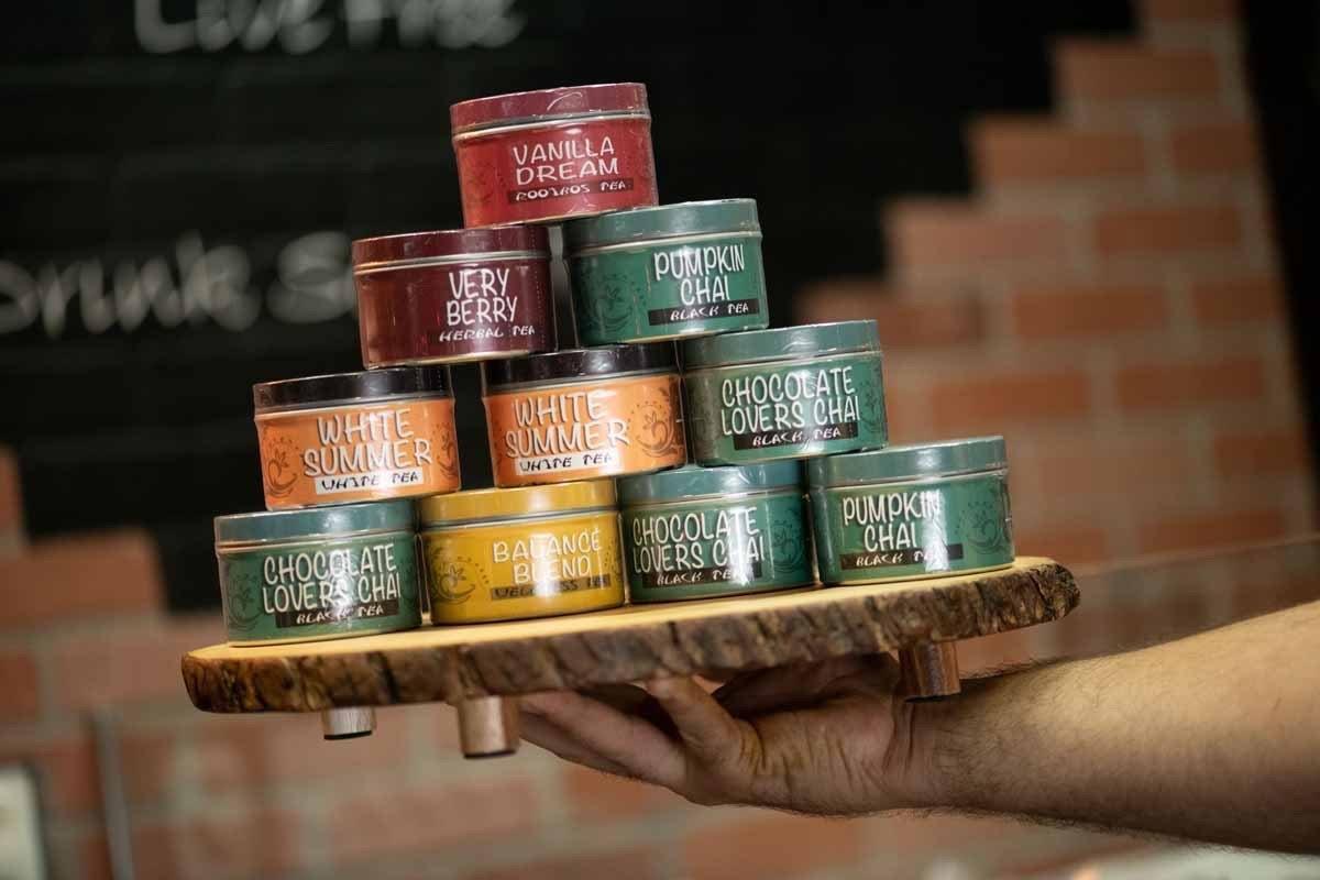 Assorted gourmet loose-leaf tea tins on a wooden tray, including chai and berry flavors