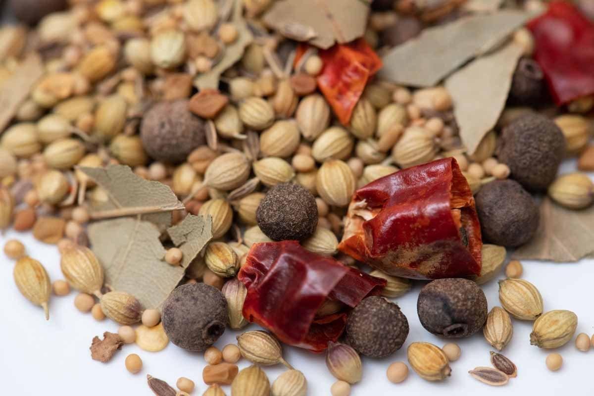 Close-up of mixed whole spices including bay leaves, coriander seeds, dried chili, and allspice.