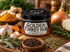 A spice blend tin labeled 'Golden Turkey Rub New York Spice Blend' sits on a rustic wooden table surrounded by ingredients including turmeric root, garlic, onions, rosemary, sage, peppercorns, and dried herbs.