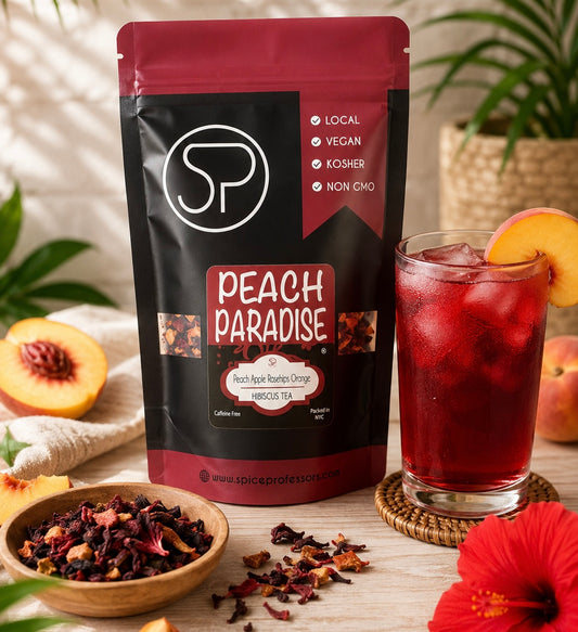 A stand-up pouch of Spice Professionals Peach Paradise hibiscus tea is shown on a tabletop beside a glass of red iced tea, with peaches, a bowl of loose tea, and tropical flowers in a styled setting.