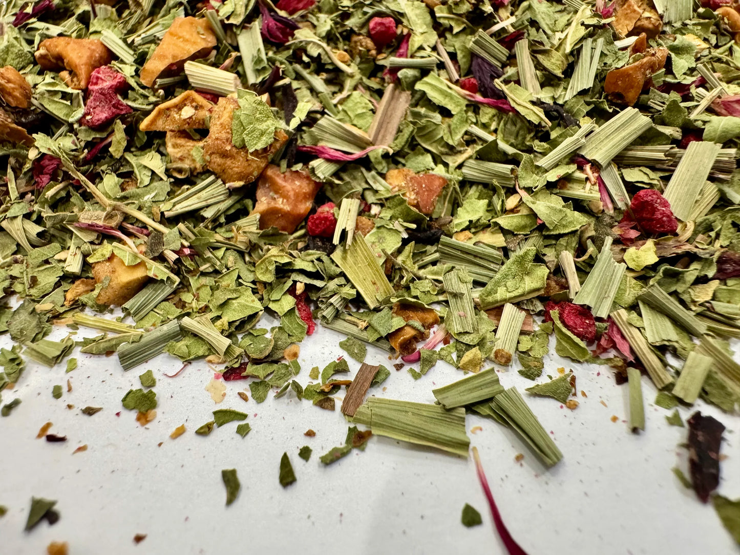 Spice mix with green herbs and red berries on a white surface