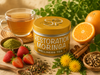 A tin of Restoration Moringa Wellness Tea is shown with a glass cup of brewed tea, strawberries, oranges, cinnamon sticks, matcha powder, and dried herbs on a rustic fabric surface.