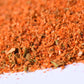 Close-up of coarse red-orange spice blend with herbs on a white surface