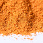 Close-up of a vibrant orange gourmet spice blend pile on a white surface