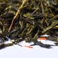 Close-up of loose leaf green tea with dried herbs on a white surface