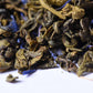 Loose-leaf green tea with dried blue petals on white background