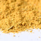 Close-up of yellow spice blend powder with visible herbs on a white surface