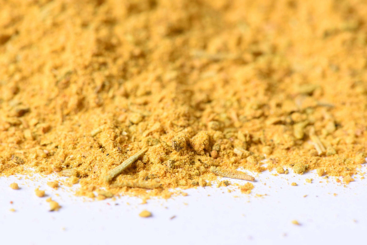 Close-up of yellow spice blend powder with visible herbs on a white surface